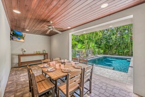 Un espace extérieur aménagé pour les repas, avec une piscine, des meubles en bois et un ventilateur de plafond.