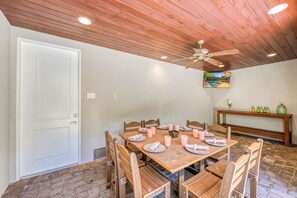 A dining area with a wooden table set for six, surrounded by chairs, a ceiling fan, and a painting on the wall.