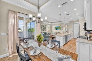 Une salle à manger spacieuse avec une grande table dressée pour six personnes, un lustre et une vue sur l’extérieur.