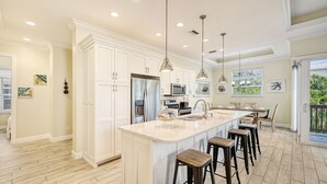 A spacious kitchen with white cabinetry, stainless steel appliances, and a large island with bar stools. - The Abalone |  Luxury Pet Friendly Home, 2 Heated Pools, Ping Pong Tables Steps to Beach! (Sarasota)