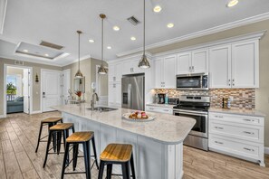 A spacious kitchen with white cabinets, stainless steel appliances, and a large island with stools.