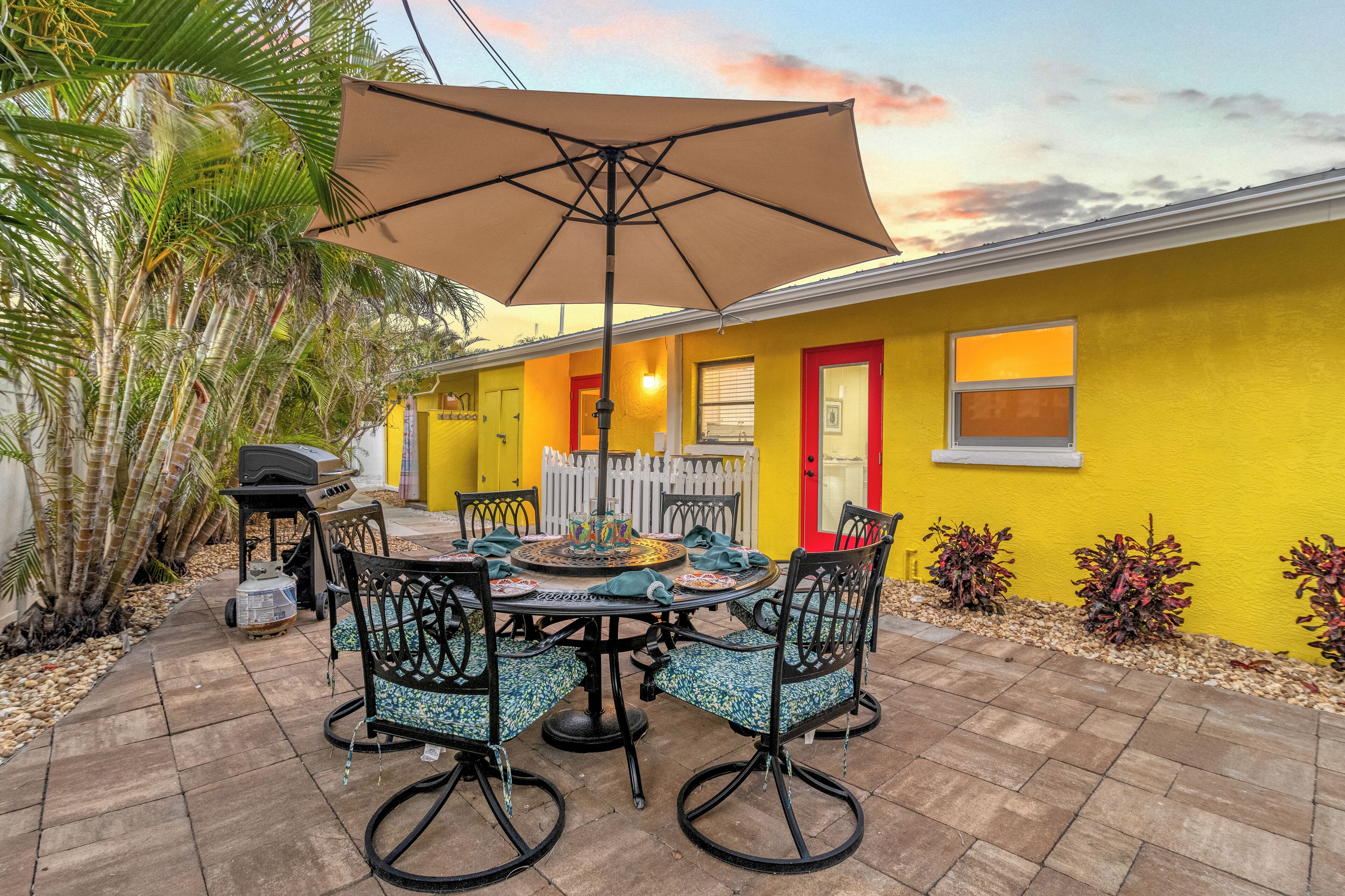 Une terrasse avec une table et des chaises, un barbecue, et un bâtiment jaune avec une porte rouge.