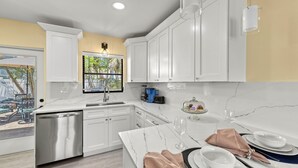 A modern kitchen with white cabinets, a marble countertop, and a dining area set for a meal. - 🌴 Sol Y Mar | Private Duplex - Two Casitas, Walk to Siesta Keys Crescent Beach, HOA Pool (Siesta Key)