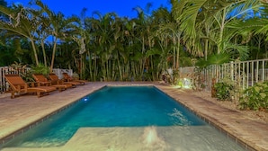 Une piscine rectangulaire à l’eau d’un bleu limpide, entourée d’une terrasse carrelée et de chaises longues en bois.