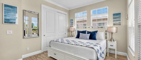 Une chambre à coucher avec un lit, un ventilateur de plafond, une fenêtre avec des stores et une table de chevet avec une lampe.