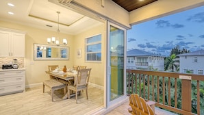 Un coin repas avec une table dressée pour quatre personnes, une cuisine avec des meubles blancs et un balcon doté d’une balustrade en bois donnant sur un quartier résidentiel.