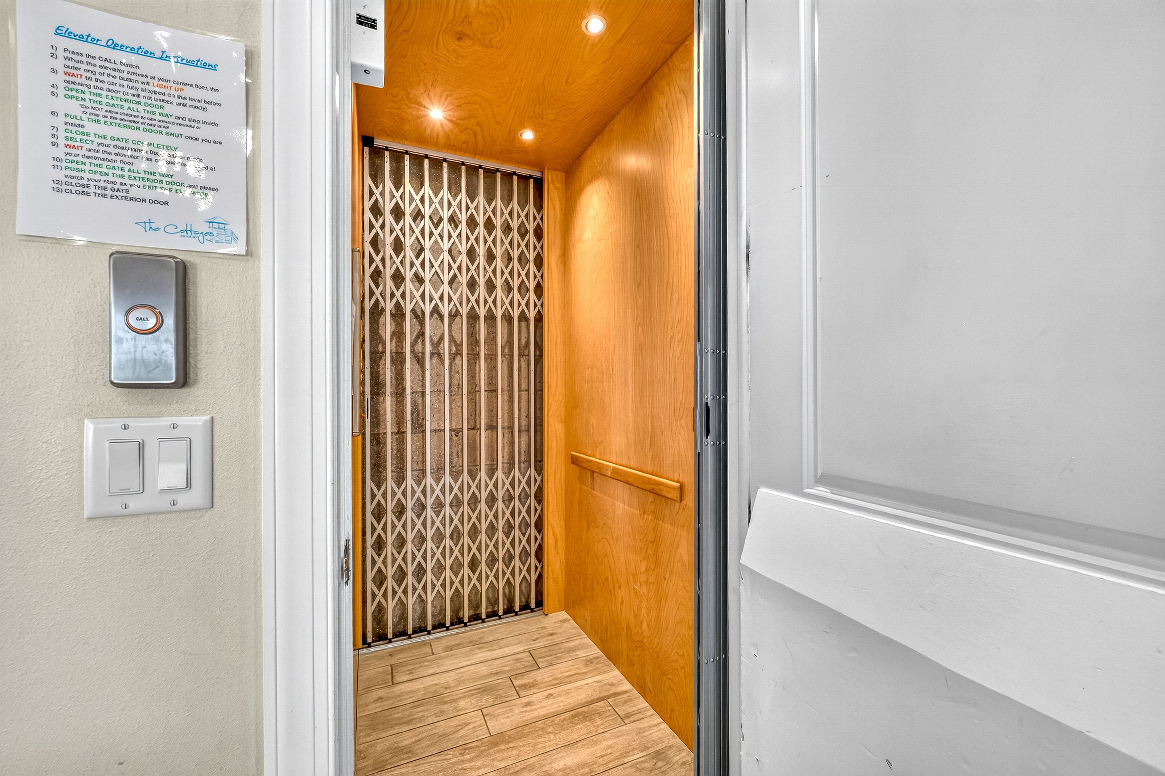 Un pasillo estrecho con piso de madera, una reja de metal y una puerta blanca.