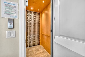 Um corredor estreito com piso de madeira, um portão de metal e uma porta branca.