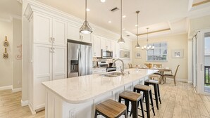 Une cuisine spacieuse avec des meubles blancs, des appareils en acier inoxydable et un grand îlot central doté de tabourets.