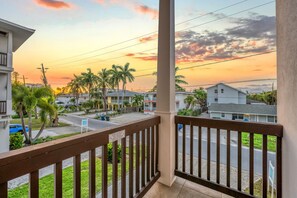 A balcony with a view of a residential street, palm trees, and houses during sunset.