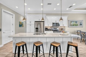 Una cocina moderna con una isla grande, electrodomésticos de acero inoxidable, iluminación colgante y taburetes de bar.