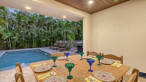 Ein Essbereich im Freien mit Pool, umgeben von üppiger Vegetation und ausgestattet mit Holztischen und -stühlen.
