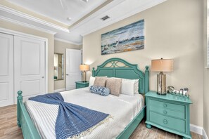 A bedroom with a bed, nightstands, a painting, and a door.