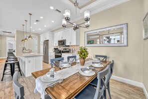 A modern kitchen with white cabinets, stainless steel appliances, and a dining area set for six with a wooden table and blue chairs.