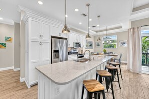 A modern kitchen with white cabinetry, stainless steel appliances, a large island with bar stools, and pendant lighting.