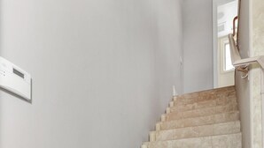Un escalier recouvert de carreaux de couleur beige et agrémenté d’appliques murales blanches.
