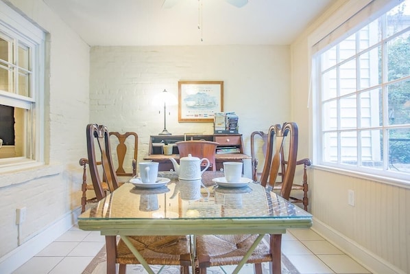 A dining area with a glass table, wooden chairs, and a view of the outdoors through a large window.