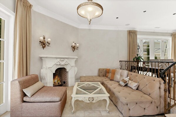 A living room with a beige sofa, a glass-top coffee table, a fireplace, and a staircase.