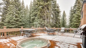 A wooden deck with a hot tub, outdoor furniture, and a view of tall evergreen trees.