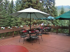 A wooden deck with outdoor tables and chairs, surrounded by a wooden railing and potted plants. - Private Home on Vail Mountain | 324W Beaver Dam (Vail)