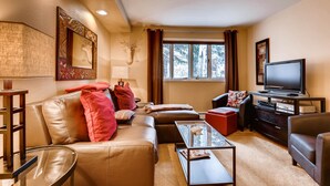 Ein gemütliches Wohnzimmer mit Ledersofas, einem Glastisch, einem Flachbildfernseher und einem aufgehängten Hirschkopf an der Wand.