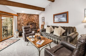 A cozy living room with a stone fireplace, leather furniture, and a framed picture on the wall. - Large top-floor Vail Condo with Views | W405 (Vail)