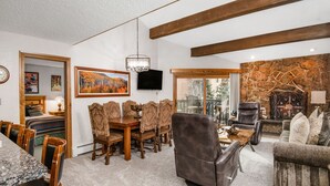 Un salón amplio con comedor, chimenea de piedra y un ventanal grande.