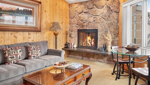 A cozy living room with a stone fireplace, wooden walls, a grey sofa, and a glass coffee table. - Vail top-floor Condo, Pool, Hot Tub | W403 (Vail)