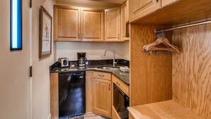 A compact kitchen with wooden cabinets, a dishwasher, a coffee maker, and a hanging clothes rack. - Ski-lodge hotel room Lionshead Village | W306B (Vail)