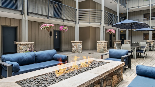 A spacious outdoor seating area with a stone fire feature, blue sofas, and hanging flower baskets. - Ski-lodge hotel room Lionshead Village | W306B (Vail)