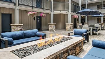 A spacious outdoor seating area with a stone fire feature, blue sofas, and hanging flower baskets.