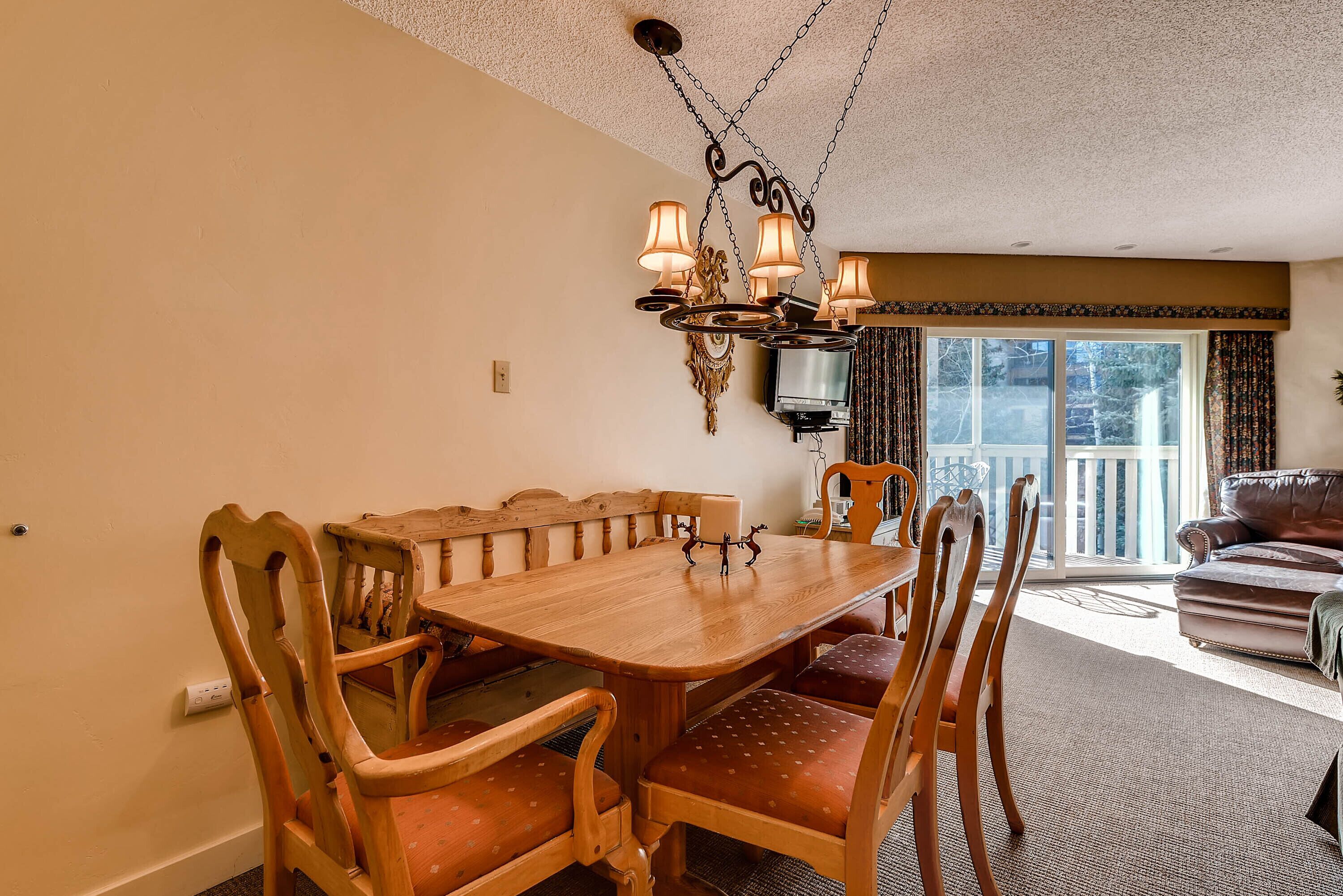 Un coin repas avec une table et des chaises en bois, un lustre et une vue sur l’extérieur par une fenêtre.