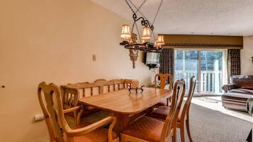 Un coin repas avec une table et des chaises en bois, un lustre et une vue sur l’extérieur par une fenêtre.