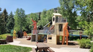 A playground with various play structures, including a slide and climbing areas, surrounded by trees and a picnic table. - Views, Bright Spacious Vail Villa, SAV4B (Vail)
