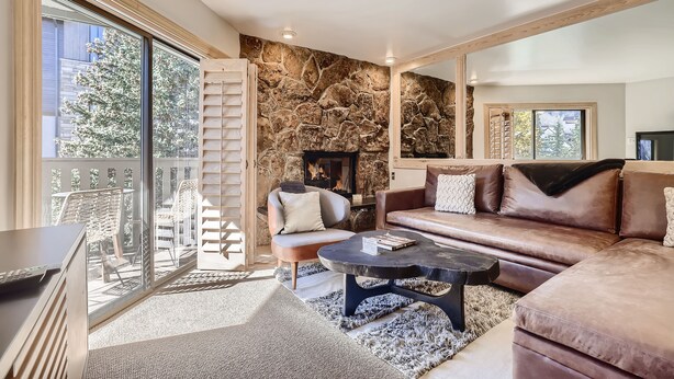 A modern living room with a stone wall, a fireplace, a leather sofa, and a glass door leading to an outdoor area. - Vail Platinum Condo in Lionshead Village W307 (Vail)