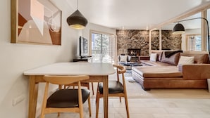 A modern living room with a dining area, stone wall, and large windows. - Vail Platinum Condo in Lionshead Village W307 (Vail)