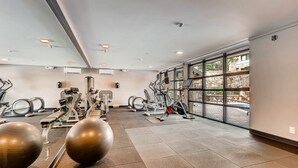 Ein Fitnessraum mit Trainingsgeräten, großen Fenstern und gefliestem Boden.