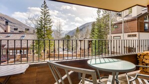 Ein Balkon mit Tisch und Stühlen mit Blick auf eine gebirgige Landschaft mit Bäumen und Gebäuden.