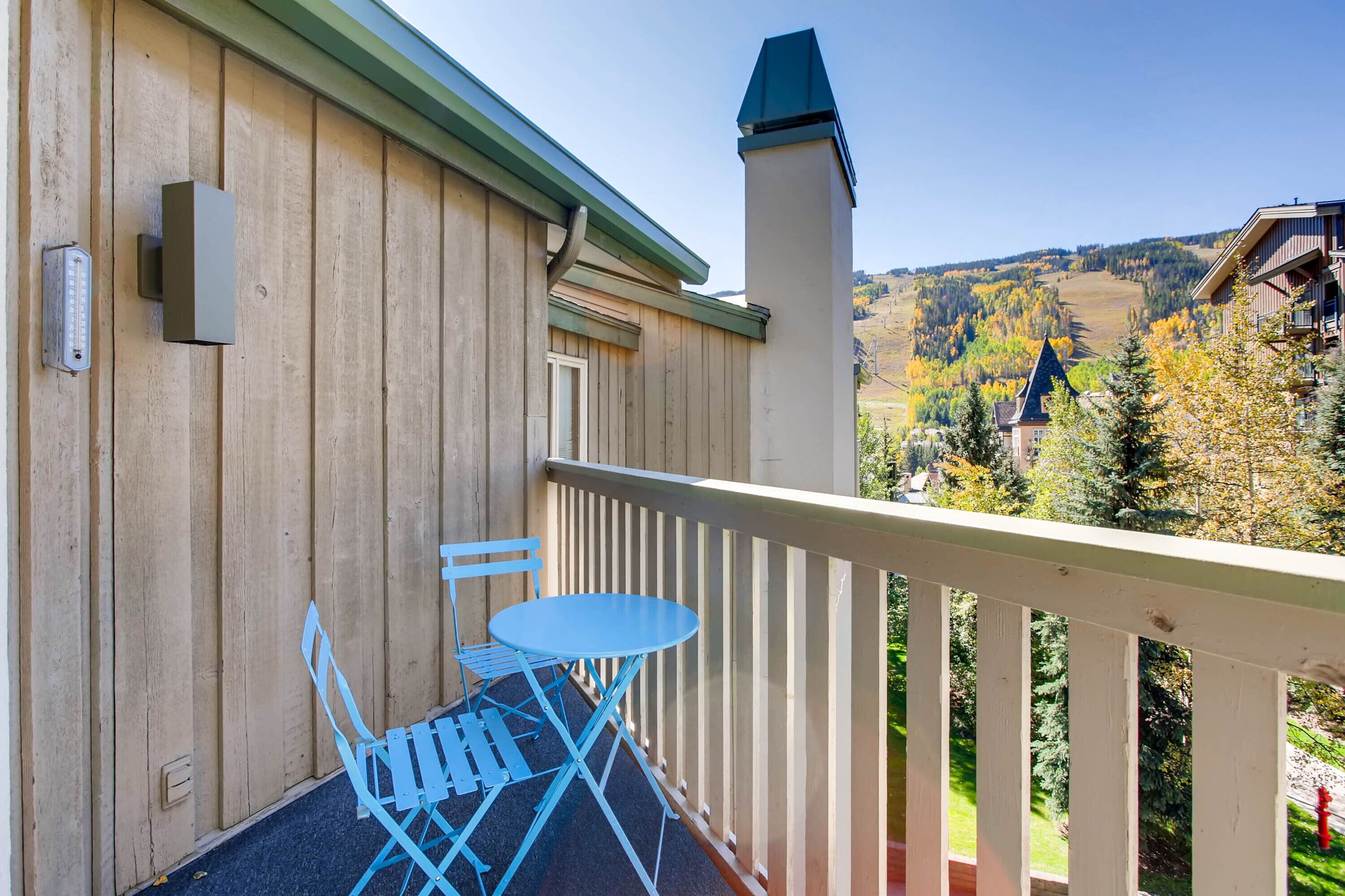 A wooden balcony with a white railing, a blue folding table, and a chair.