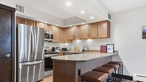 Een moderne keuken met roestvrijstalen apparatuur, houten kastjes en een centraal eiland met barkrukken.