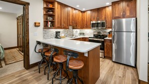 Une cuisine moderne avec des meubles en bois, un réfrigérateur en acier inoxydable et un îlot central doté de tabourets de bar.
