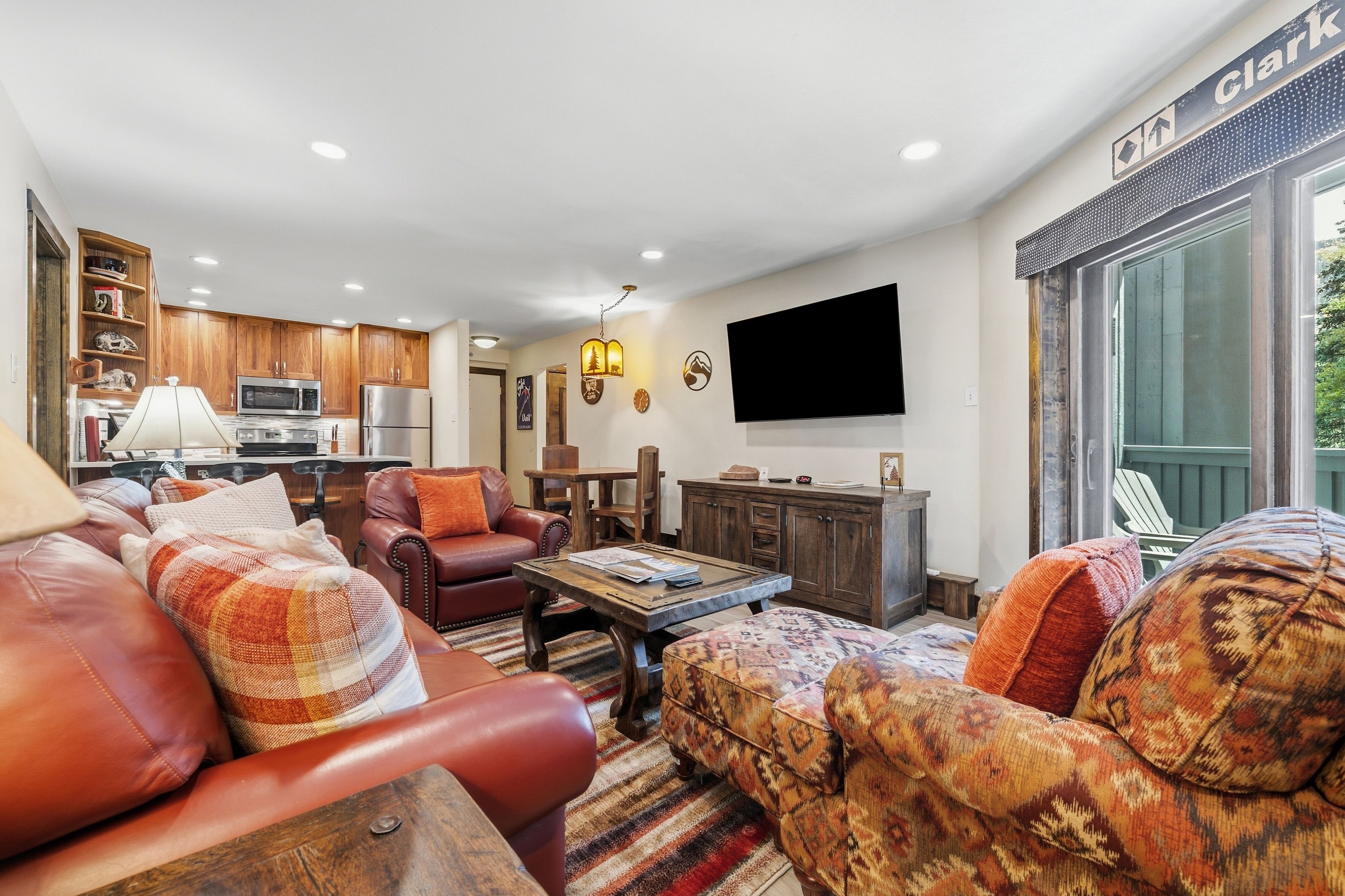 A modern living room with leather sofas, a wooden coffee table, and a flat-screen TV mounted on the wall.