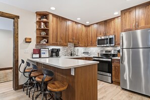 A modern kitchen with wooden cabinets, stainless steel appliances, a central island with bar stools, and a tiled backsplash. - Luxury Condo, Pool, Hot Tub, near Gondola | W108 (Vail)