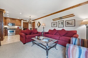 A modern living room with two red sofas, a glass coffee table, and a kitchen in the background. - Remodeled Condo Vail Mtn Views | W201 (Vail)