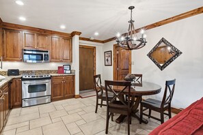 A kitchen with wooden cabinets, a stainless steel oven, a microwave, and a dining area with a round table and chairs. - Remodeled Condo Vail Mtn Views | W201 (Vail)