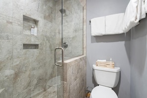Casa de banho moderna com cabine de duche de vidro, azulejos de mármore, sanita branca e um porta-toalhas.