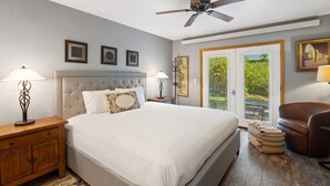 Un dormitorio con cama, mesitas de noche, ventilador de techo y vistas por la puerta.