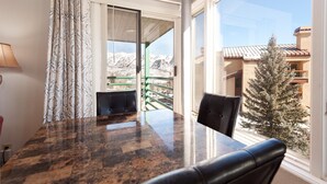 Ein Zimmer mit Glastisch und -stühlen, Blick auf schneebedeckte Berge und ein Balkon mit Geländer.