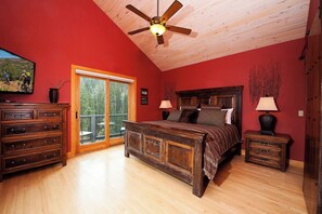 Une chambre avec un ventilateur de plafond en bois, un grand lit avec une literie à motifs, une commode et une table de chevet avec des lampes.