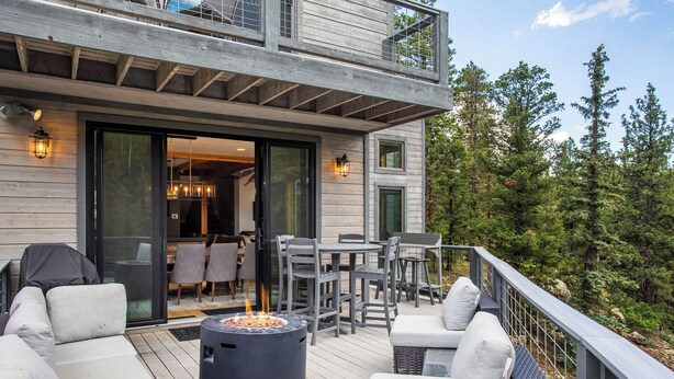 Una terraza con mobiliario exterior, una fogata y vistas a una zona boscosa.